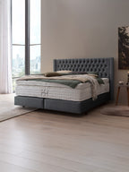 Ein luxuriöses Boxspringbett mit grauem Kopfteil und weißer Matratze in einem modernen Schlafzimmer.