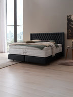 Schwarzes Boxspringbett mit gestepptem Kopfteil und weißer Matratze in einem modernen Schlafzimmer.