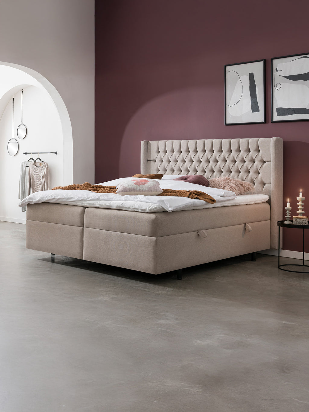 Ein Schlafzimmer mit einem beigen Boxspringbett, lila Wänden und einem begehbaren Kleiderschrank.