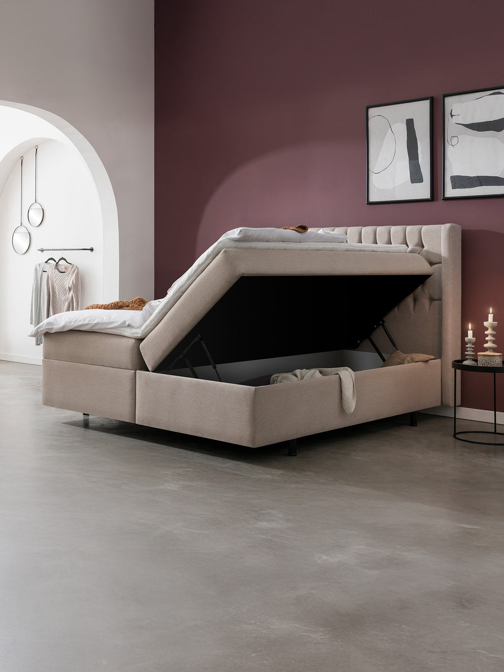 Beigefarbenes Boxspringbett mit offenem Stauraum in einem modernen Schlafzimmer mit lila Wand und Bogen.