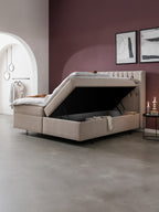 Beigefarbenes Boxspringbett mit offenem Stauraum in einem modernen Schlafzimmer mit lila Wand und Bogen.