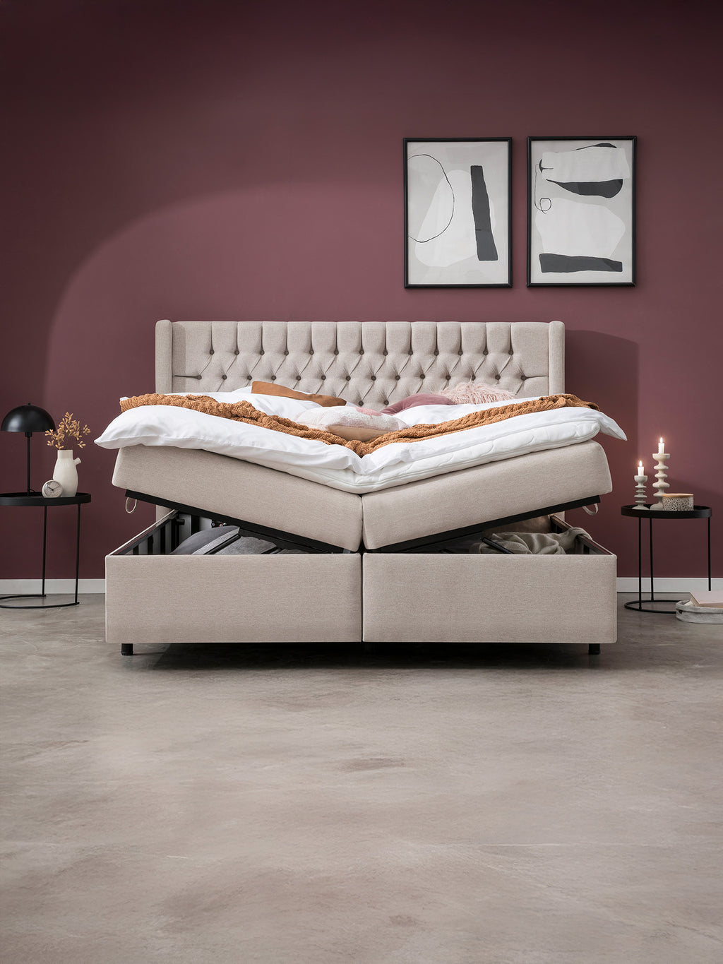 Ein beiges Boxspringbett mit Stauraum, der geöffnet ist, steht in einem Schlafzimmer mit weinroten Wänden.
