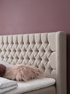 Gepolstertes Kopfteil mit Knöpfen und zwei Kissen auf einem Bett.