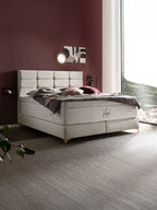 Ein luxuriöses Schlafzimmer mit einem großen, beigefarbenen Boxspringbett und einer weinroten Wand.