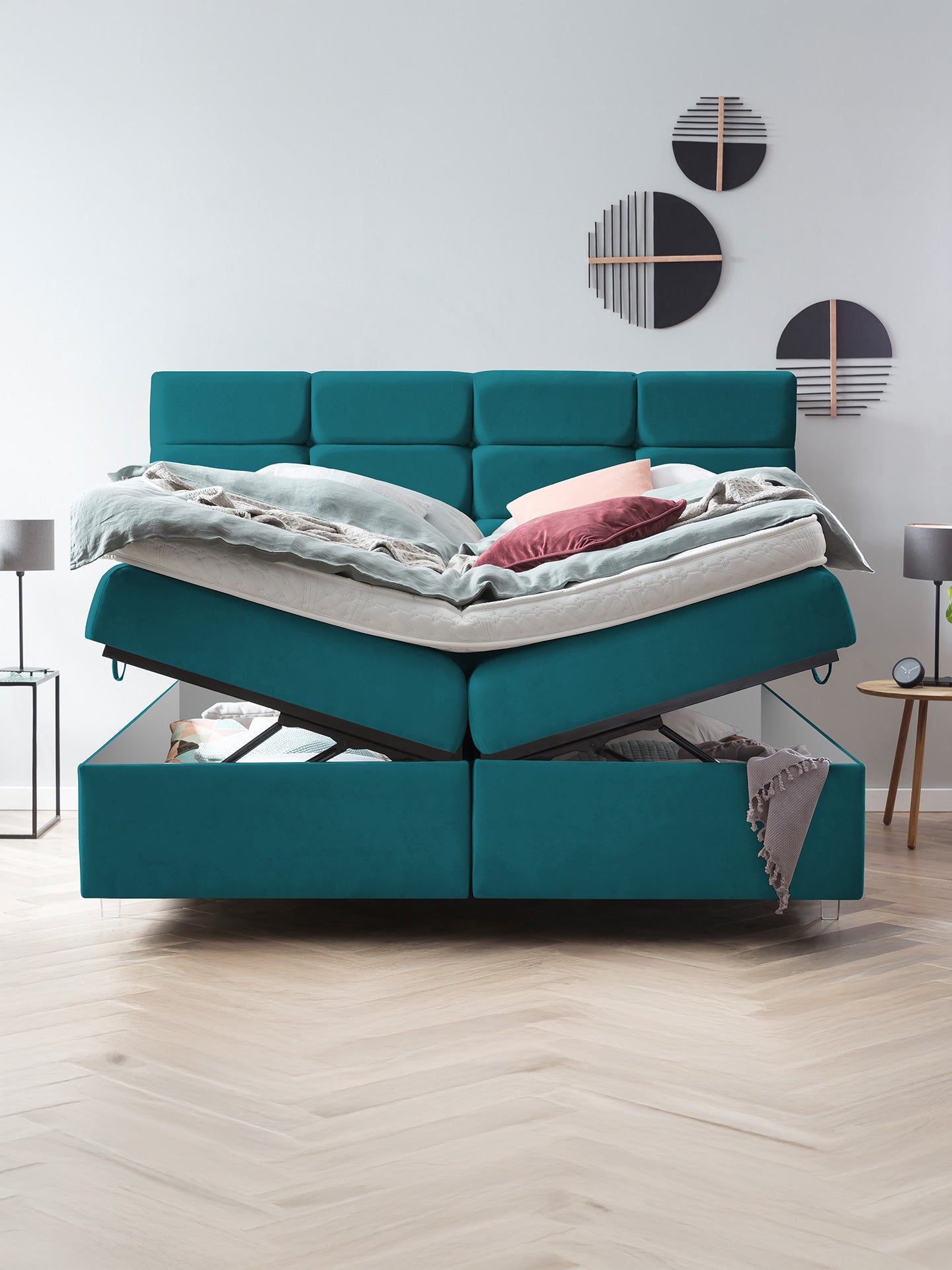 Ein tealgrünes Boxspringbett mit offenem Stauraum unter der Matratze.
