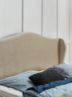 Ein beiges Kopfteil mit blauen Kissen und einer blauen Decke auf einem Bett.