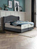 Ein elegantes Schlafzimmer mit einem grauen Boxspringbett, blauer Bettwäsche und Kunstwerken an der Wand.