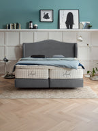 Ein modernes Schlafzimmer mit einem grauen Boxspringbett und blauer Bettwäsche. Die Wände sind türkis und weiß getäfelt.