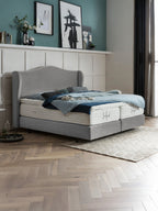 Graues Boxspringbett mit blauer Bettwäsche in einem Schlafzimmer mit Fischgrätparkett und Kunstwerken an der Wand.