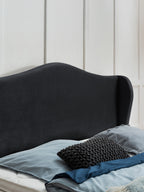 Schwarzes Kopfteil mit blauen Kissen und Decke auf einem Bett.