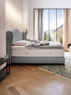 Ein Schlafzimmer mit einem grauen Bett, einem BettCo Topper und Blick auf eine Berglandschaft.