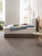 Ein Schlafzimmer mit einem Bett, das ein BettCo-Logo auf der Matratze hat. Das Bett ist mit blauen Kissen und einer Decke dekoriert.