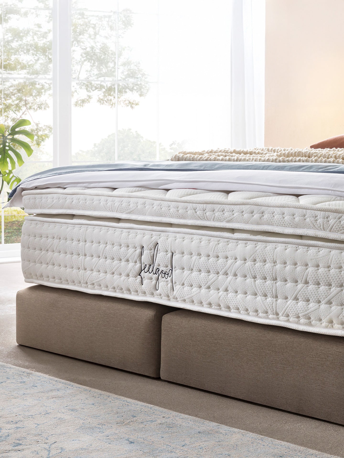 Nahaufnahme einer weißen Matratze mit dem Schriftzug feelgood in einem hellen Schlafzimmer.