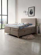 Modernes Boxspringbett mit beigem Kopfteil und blauer Bettwäsche in einem hellen Schlafzimmer.