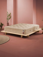 Beigefarbene Matratze auf einem niedrigen Holzrahmenbett in einem Raum mit rosa Wänden und Terrakottaboden.