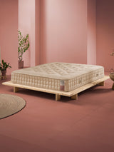 Beigefarbene Matratze auf einem niedrigen Holzrahmenbett in einem Raum mit rosa Wänden und Terrakottaboden.