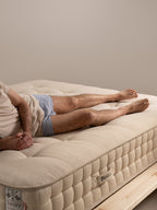 Ein Mann liegt auf einer beigen Matratze mit dem Bett&Co-Logo, seine Hände sind gefaltet.